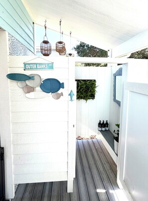 A covered porch with a sign reading 'Outer Banks Hwy,' decorative fish sculptures, hanging lanterns, and a wooden deck.