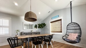A dining area with a wooden table, black chairs, a hanging chair, and a large mirror.