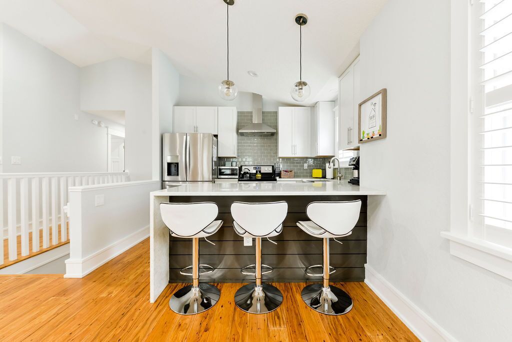 A modern kitchen with white cabinetry, a central island with bar stools, stainless steel appliances, and pendant lighting.