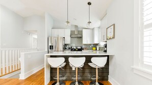 A modern kitchen with white cabinetry, a central island with bar stools, stainless steel appliances, and pendant lighting.