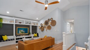 A modern living room with a brown sofa, a ceiling fan, and a wall decorated with woven baskets.