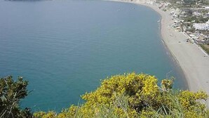 A coastal view with a beach, a small island, and a mountainous backdrop.