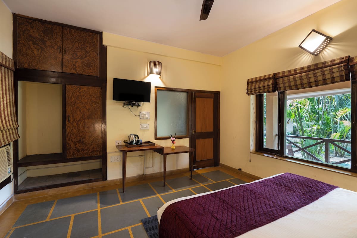 Habitación de hotel con una cama, un escritorio con lámpara, un televisor y una ventana con vistas a zonas verdes.