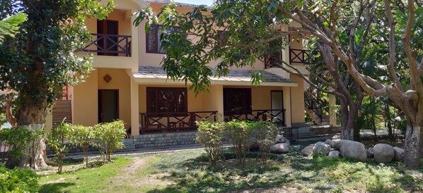 A two-story building with a balcony, surrounded by trees and rocks. - Corbett Wild Resort - A River Access Property (Ramnagar)