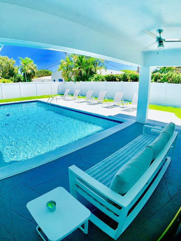 A pool area with a seating area, including a sofa and a table, and a ceiling fan.