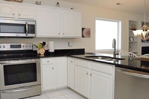 Features a kitchen with stainless steel appliances, white cabinetry, and a black countertop, including a microwave, oven, and sink.