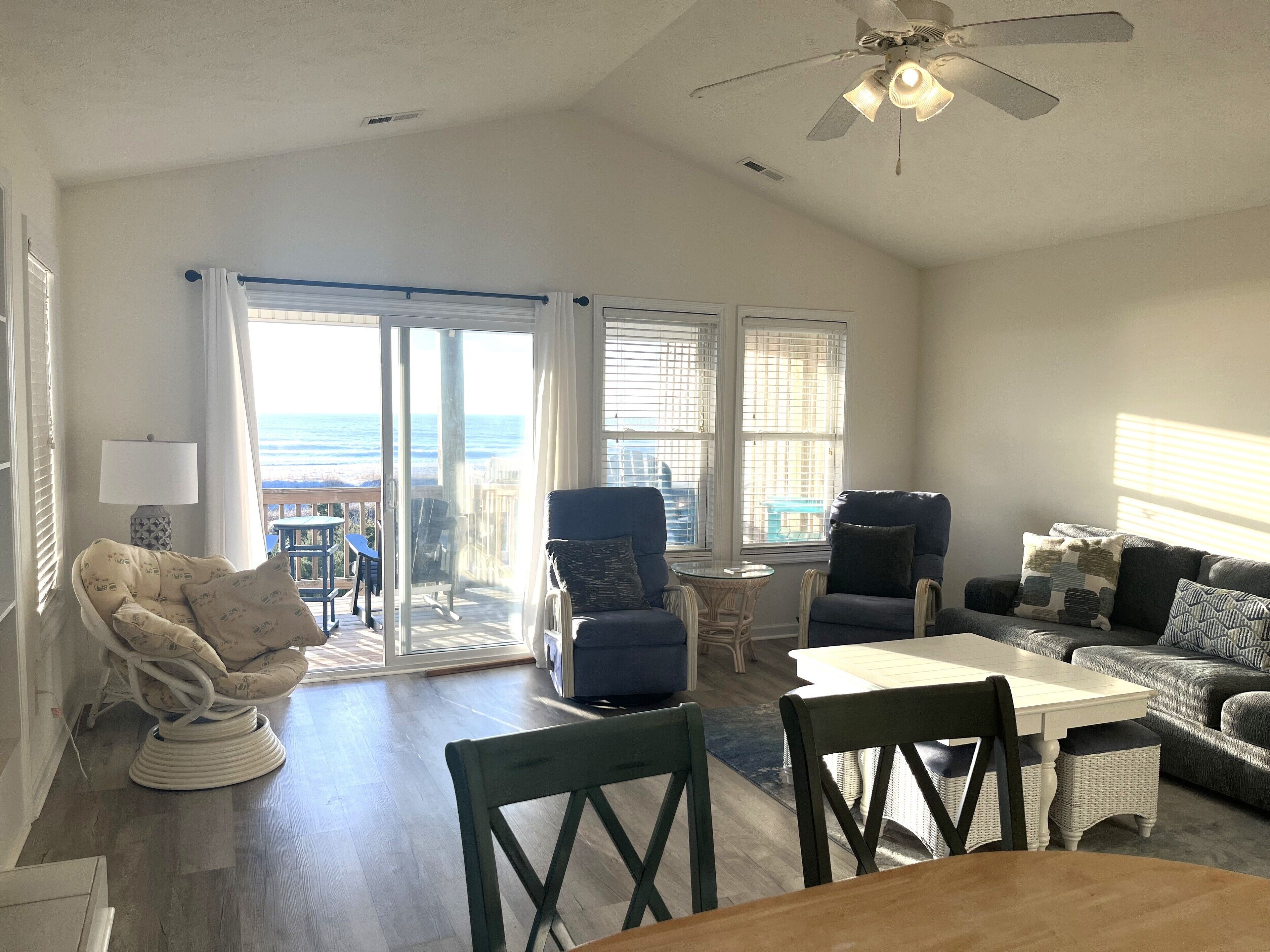 A spacious living room with a view of the ocean, a ceiling fan, and a dining area with a table and chairs.