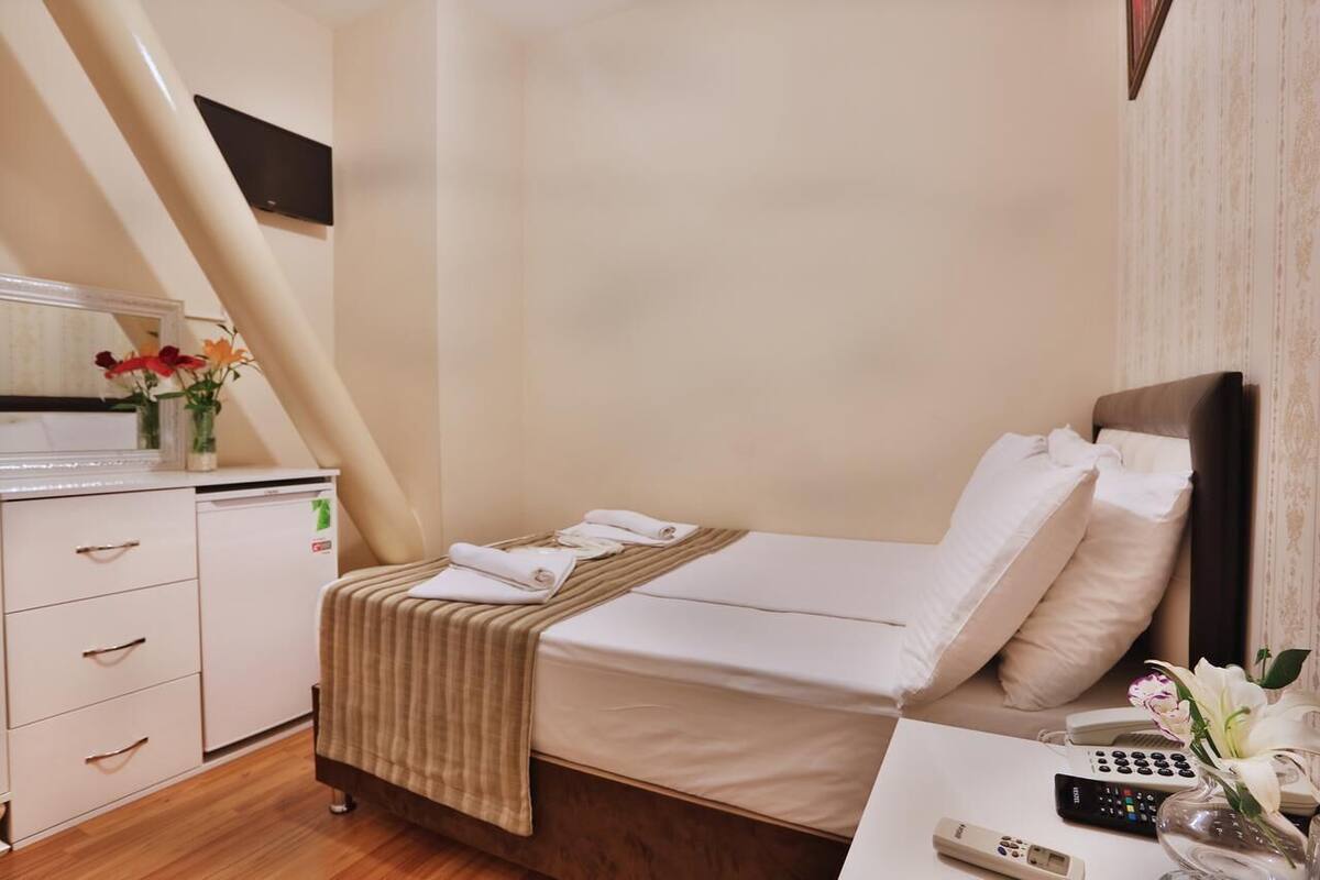 A hotel room with a bed, bedside table, and a small desk with a telephone and remote controls.