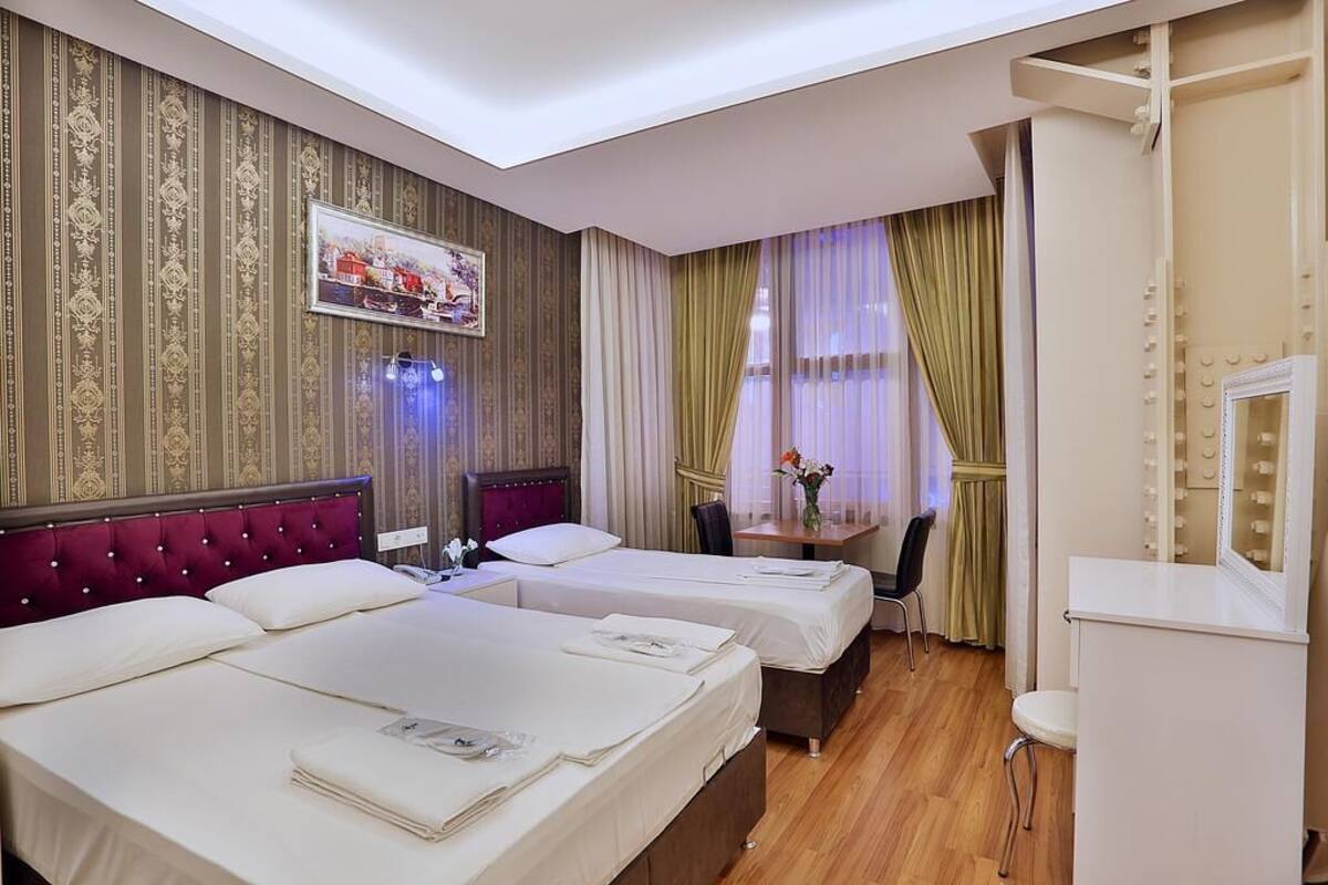 A hotel room with two beds, a vanity with a mirror, and a small table with a vase of flowers.