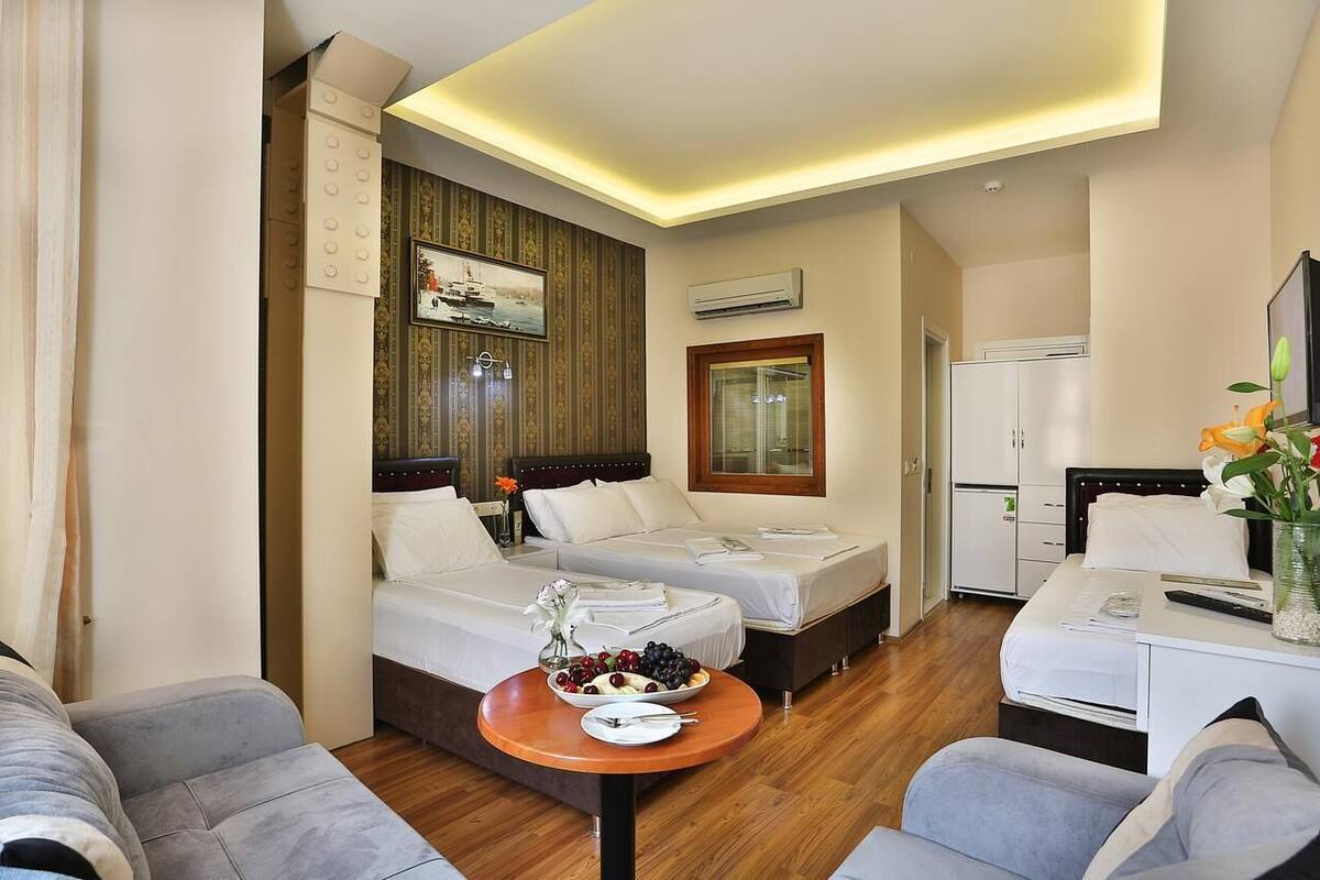 A hotel room with two beds, a dining table with fruit, a TV, and a window.
