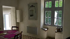 Una habitación con cama, silla, ventana con múltiples vidrios, espejo y radiador.