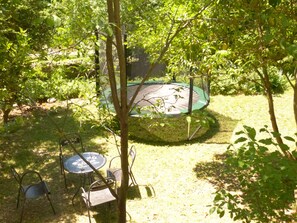 A trampoline surrounded by trees and grass, with metal chairs and a table nearby. - Iris On a hillside gite sleeps 4 Mas EDEN Unobstructed view (Thoiras)