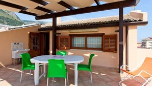 An outdoor patio with a table and chairs, a grill, and a view of the mountains.