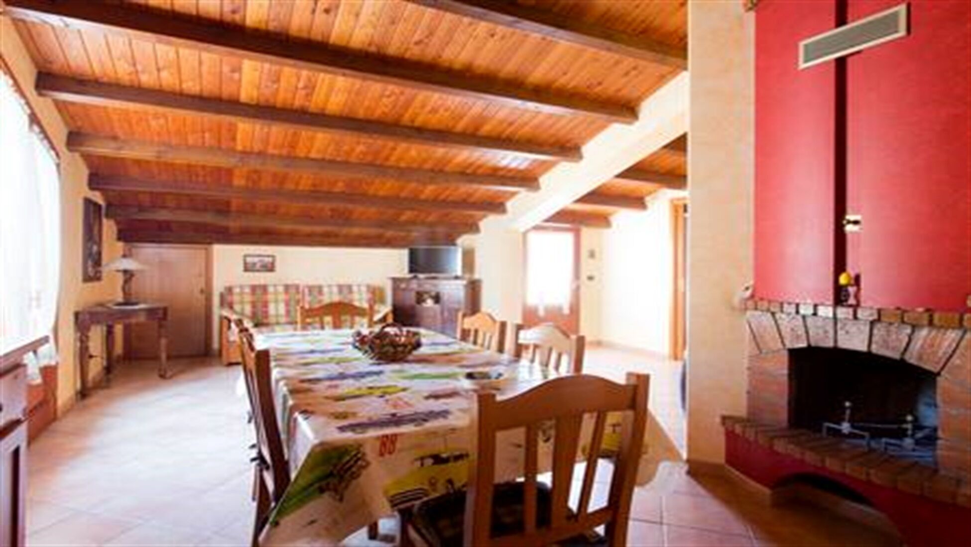Un comedor con techo de madera, chimenea y una mesa lista para cuatro.
