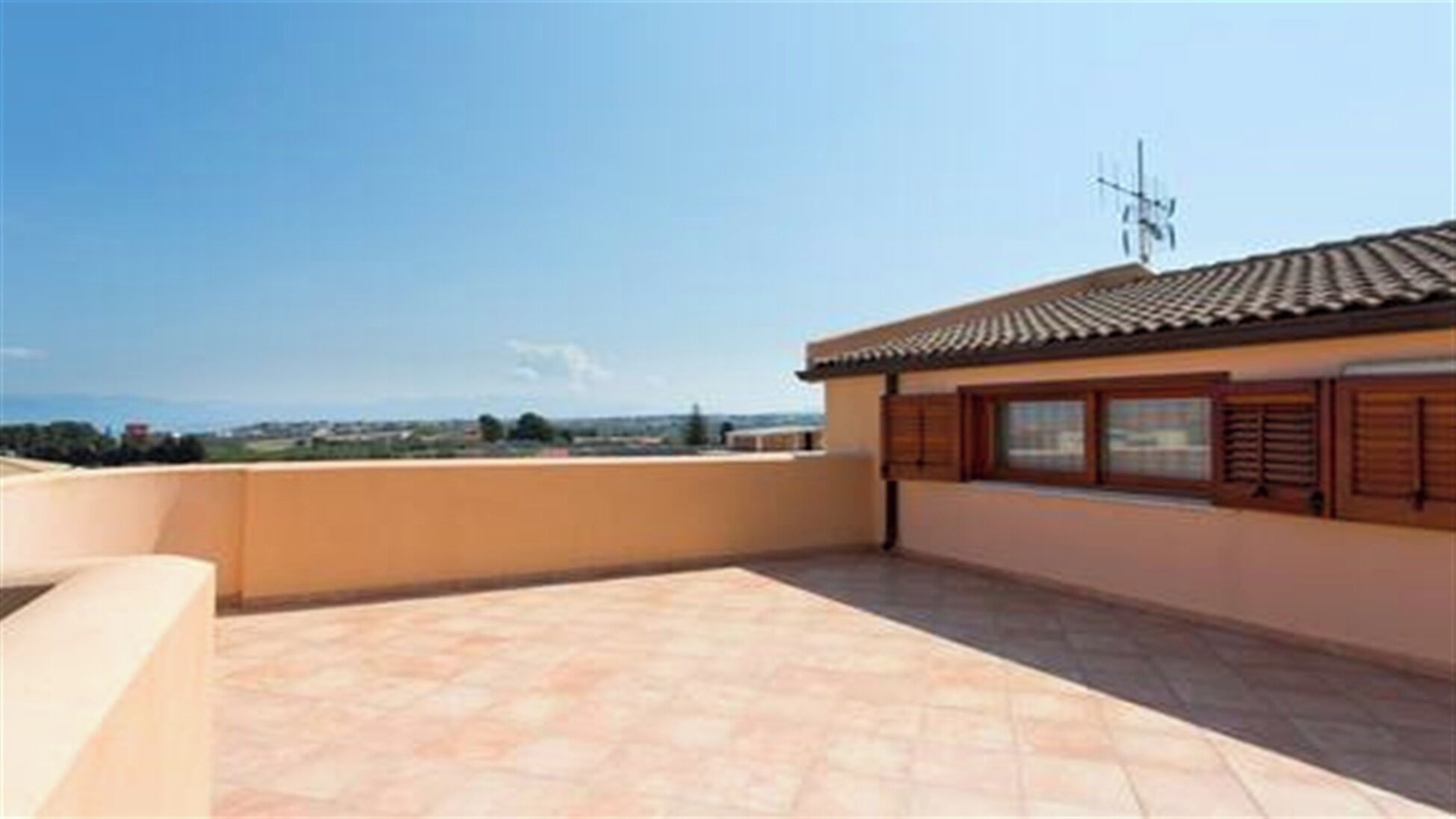 A rooftop terrace with a tiled floor, a view of the countryside, and a traditional tiled roof.