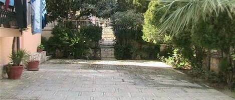 A paved courtyard with potted plants and a stone wall in the background.