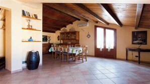 A dining area with a wooden table and chairs, a tiled floor, a wooden ceiling, and a door with windows.