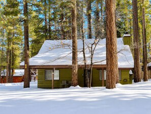 A cabin with a snow-covered roof, surrounded by tall pine trees.