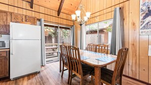 A wooden-paneled room with a dining table, chairs, a refrigerator, and a window with curtains. - Bear Crossing - Walk to Slopes, Foosball Table, Barbecue (Big Bear Lake)