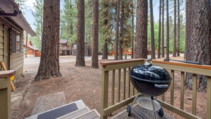 A wooden deck with a barbecue grill, surrounded by tall pine trees. - Bear Crossing - Walk to Slopes, Foosball Table, Barbecue (Big Bear Lake)