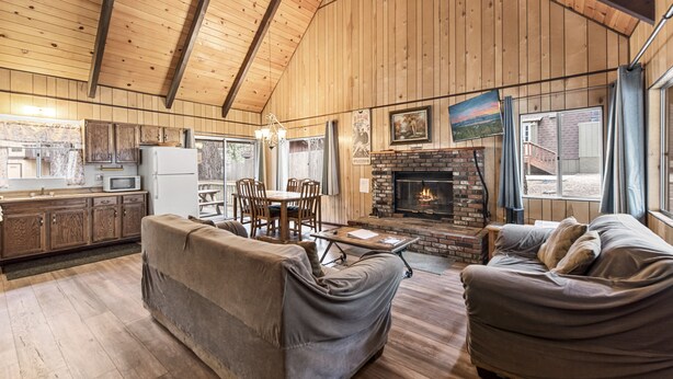 A cozy cabin interior with a dining area, two sofas, a fireplace, and wooden walls. - Bear Crossing - Walk to Slopes, Foosball Table, Barbecue (Big Bear Lake)