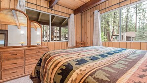 A wooden cabin bedroom with a large bed, a dresser with drawers, a mirror, and a window with curtains. - Bear Crossing - Walk to Slopes, Foosball Table, Barbecue (Big Bear Lake)