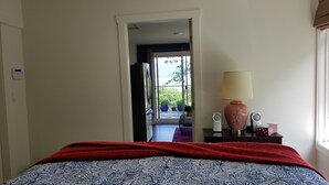 A hotel room with a bed, a red blanket, a patterned bedspread, a lamp, and a view of the balcony with potted plants. - Your private getaway! (Gibsons)