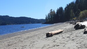 A beach with a clear sky, calm water, and a forested hillside. - Your private getaway! (Gibsons)