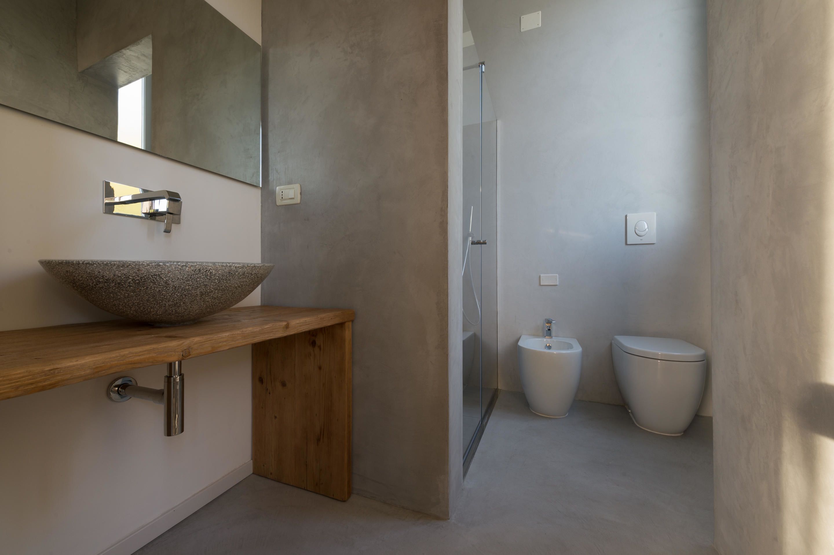 A modern bathroom with a large stone basin, a wooden countertop, a glass shower enclosure, and two toilets.
