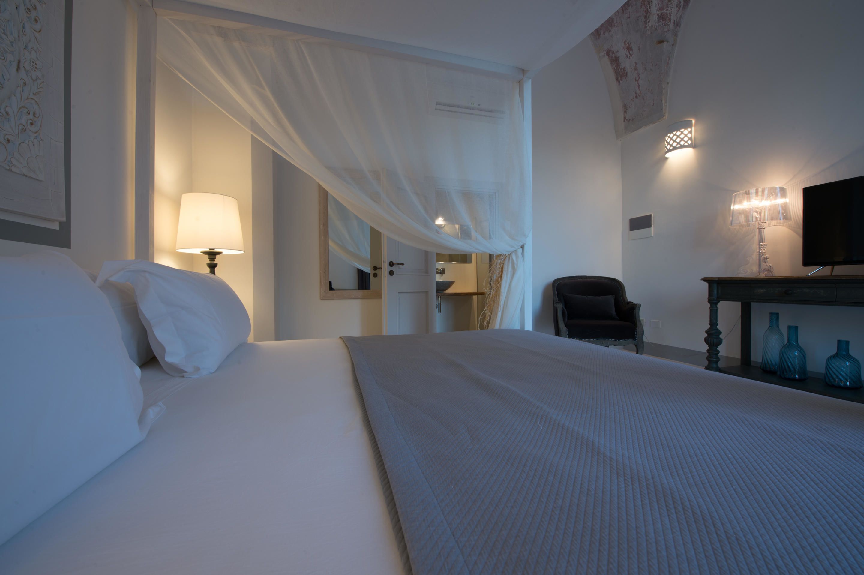 A hotel room with a large bed, a chair, a desk with blue vases, and a television.
