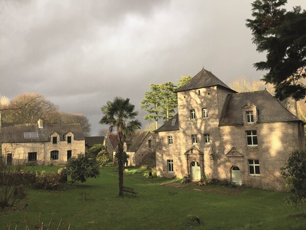 A stone building with multiple windows and a central entrance, surrounded by a grassy area and trees.
