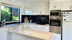 Een moderne keuken met witte kasten, een roestvrijstalen fornuis, een oven, een magnetron, en een groot raam dat natuurlijk licht binnenlaat.