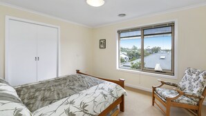 A bedroom with a bed, a chair, a window with a view, and a door. - Cavalier (Zeally Bay Rd): 4  BR, 2  BA House in Torquay, Sleeps 9 (Torquay)