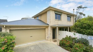A two-story house with a garage, a covered driveway, and a fenced yard with flowering plants. - Cavalier (Zeally Bay Rd): 4  BR, 2  BA House in Torquay, Sleeps 9 (Torquay)