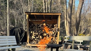 A campfire surrounded by rocks and logs, with a covered bench and picnic table nearby.