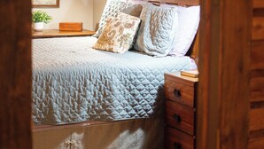 A bedroom with a bed, wooden nightstands, a wall-mounted lamp, a map, and a small plant on a shelf.