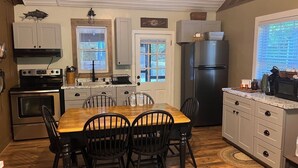 A kitchen with a wooden dining table, four chairs, a refrigerator, and a stove.