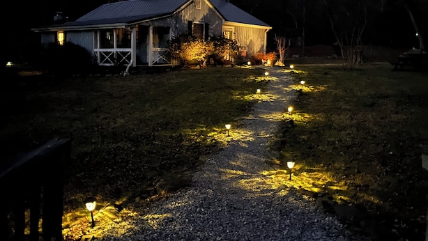 A house with a sloped roof, a front porch, and a pathway lit by ground lights.