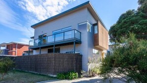 Een modern huis met twee verdiepingen, een balkon, een houten omheining en een verzorgd gazon.