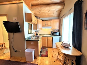 A compact kitchen with wooden cabinets, a microwave, a sink, and a small dining area with a table and chairs. - #2 Trout Cabin at Ponderosa Place (Custer)