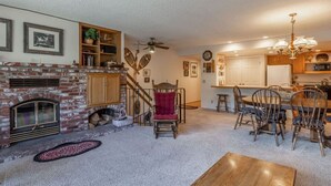 Un salon chaleureux avec une cheminée, un coin repas avec des chaises en bois et une cuisine avec des meubles blancs.