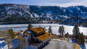Un bâtiment à deux étages, doté d’un toit en pente, d’un parking et offrant une vue sur un lac gelé et des montagnes en arrière-plan.