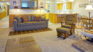 A living room with a sofa, armchair, and ottoman, a dining area with wooden chairs, and a kitchen in the background. - June Lake Interlaken 12 Cozy, Spacious (June Lake)