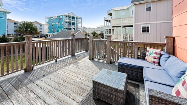 A wooden deck with outdoor furniture, a railing, and a view of multi-story buildings. - 710 Canal Upper - Make Everyday a Holiday! (Carolina Beach)