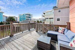 A wooden deck with outdoor furniture, a railing, and a view of multi-story buildings.