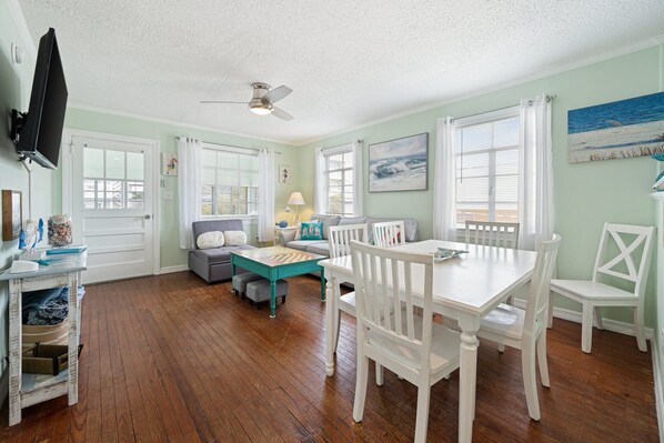 A dining area with a white table and chairs, a ceiling fan, and a view of the ocean through windows.