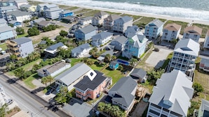 An aerial view of a coastal residential area with multiple two-story houses, a beach in the background, and a road running parallel to the houses. - 710 Canal Upper - Make Everyday a Holiday! (Carolina Beach)