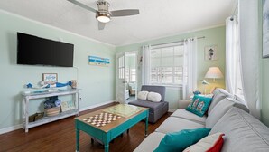A living room with a television, a ceiling fan, a coffee table, a sofa, and a window with curtains. - 710 Canal Upper - Make Everyday a Holiday! (Carolina Beach)
