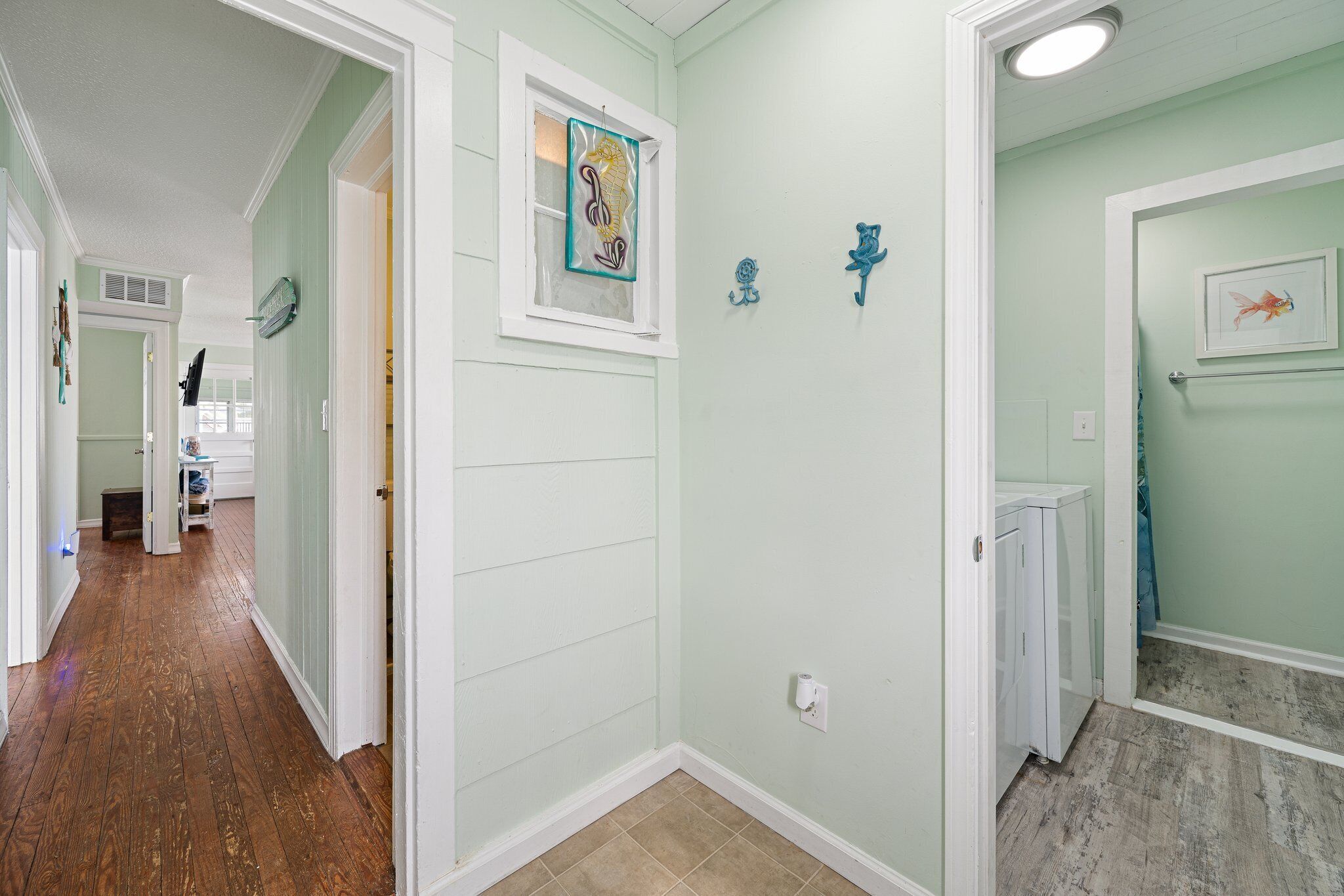 A hallway with a wooden floor, light green walls, and a window with artwork.