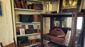 A wooden chair and a glass-fronted cabinet with shelves containing books, decorative items, and a lamp.